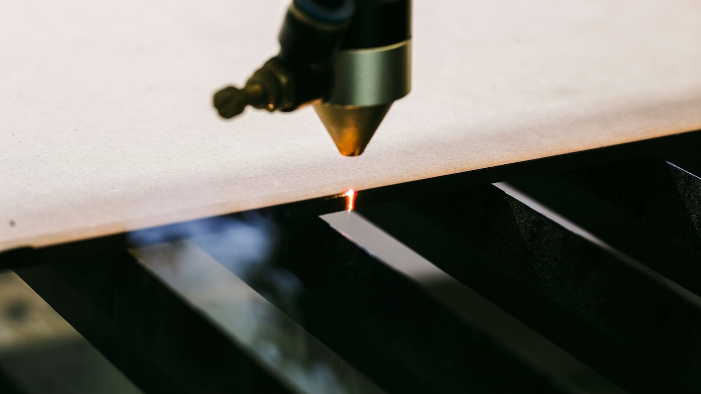 Laser cutter precisely slicing through a light-colored sheet material.