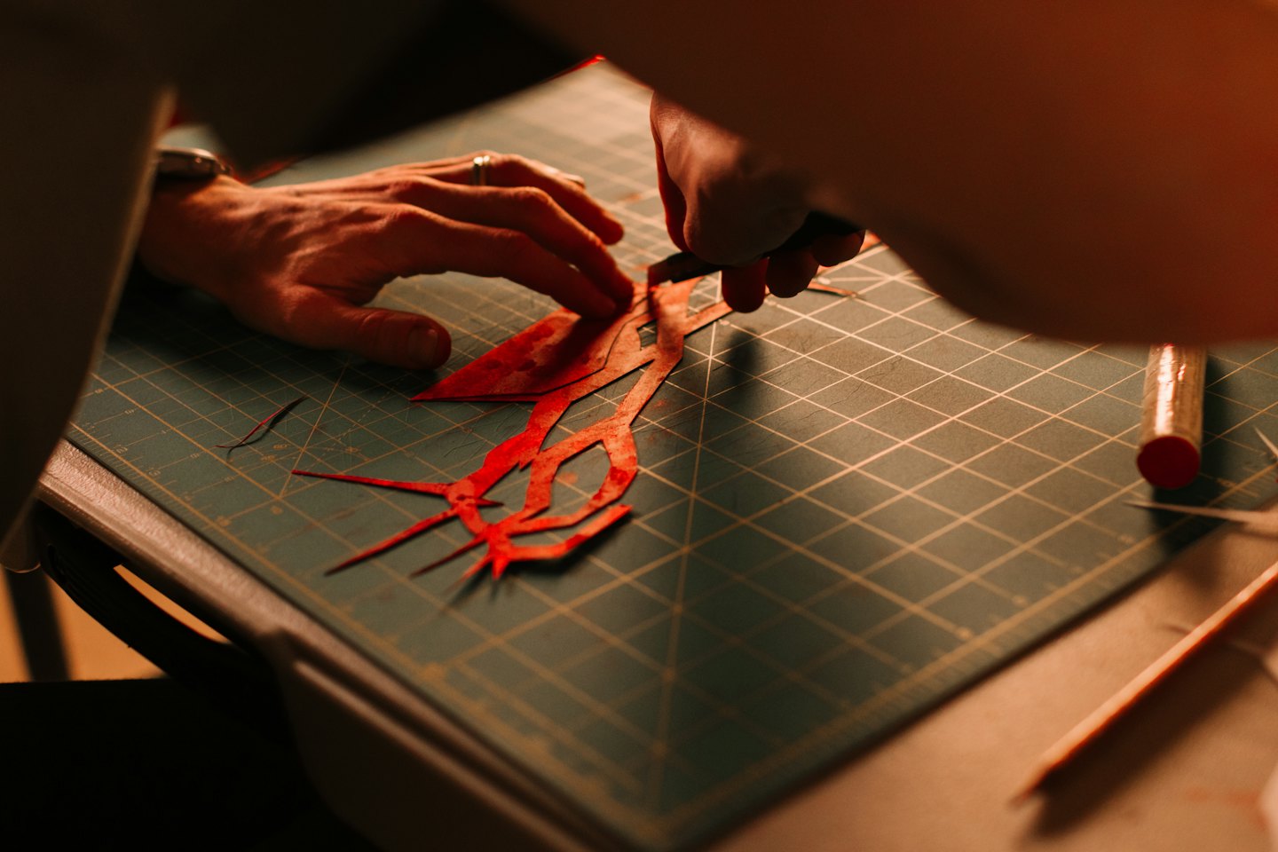 Hands cutting red paper shapes with a craft knife.