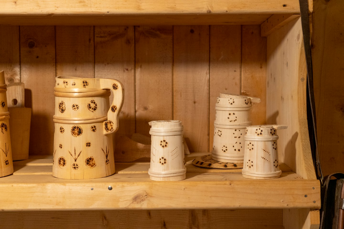 Handcrafted wooden mugs with decorative patterns sit on wooden shelves.